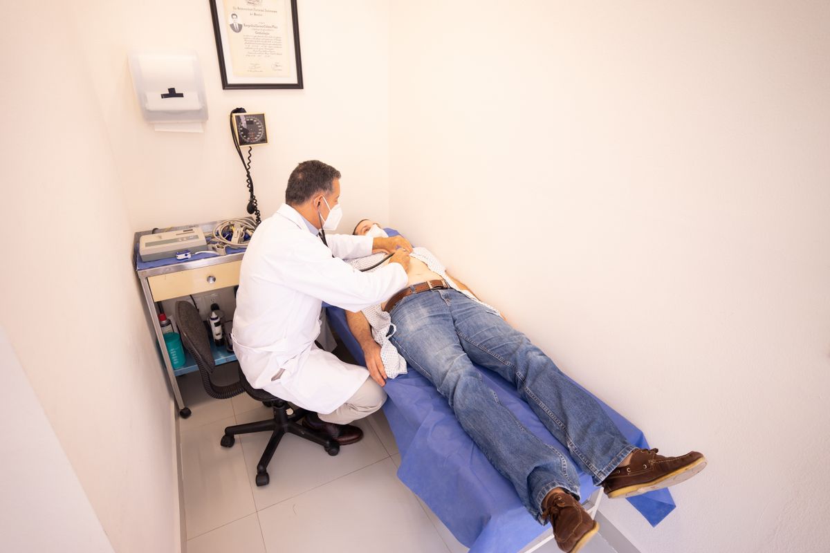 Médico auscultando o abdômen de um paciente deitado na maca